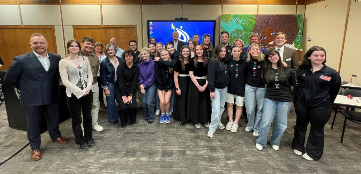 Several students gather with a handful of adults to pose for a group photo in the school board meeting room.
