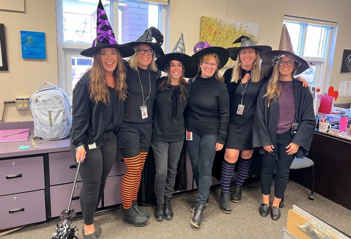 Six teacher pose in a middle school classroom while wearing witch costumes.