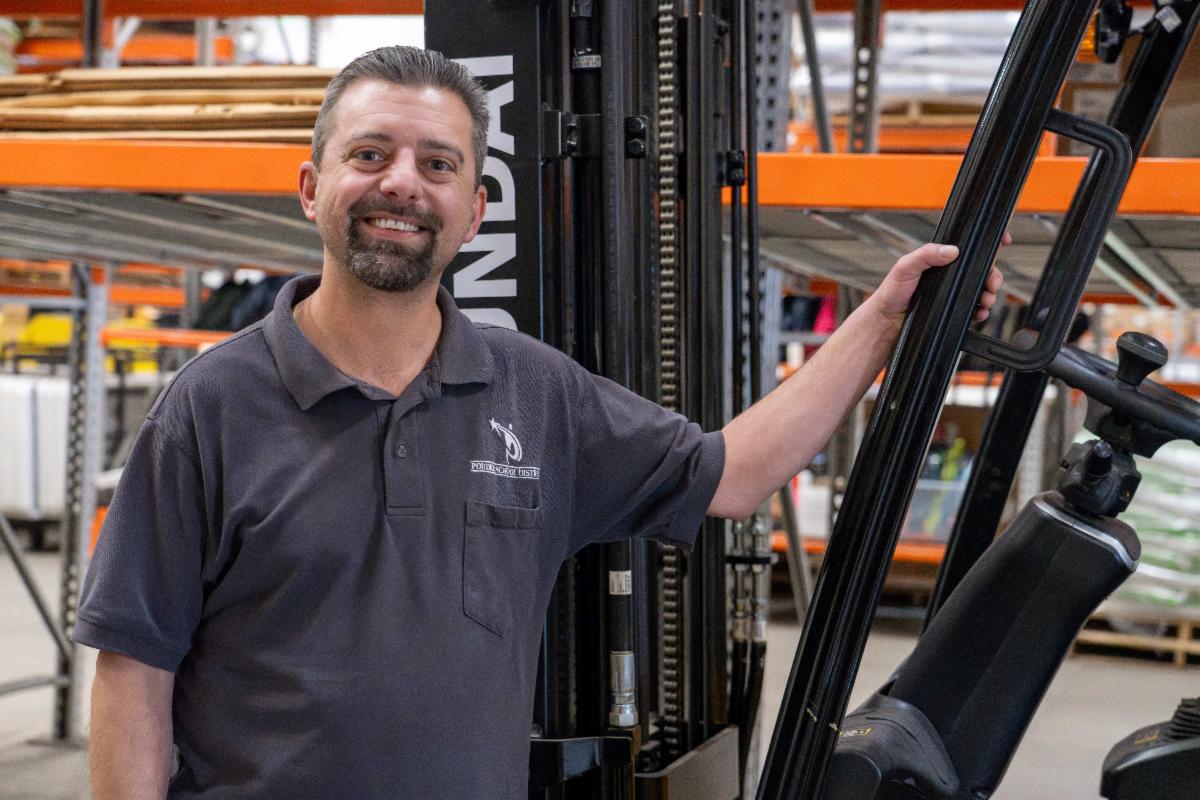 Portrait photo of a man standing and putting his hand on a forklift.