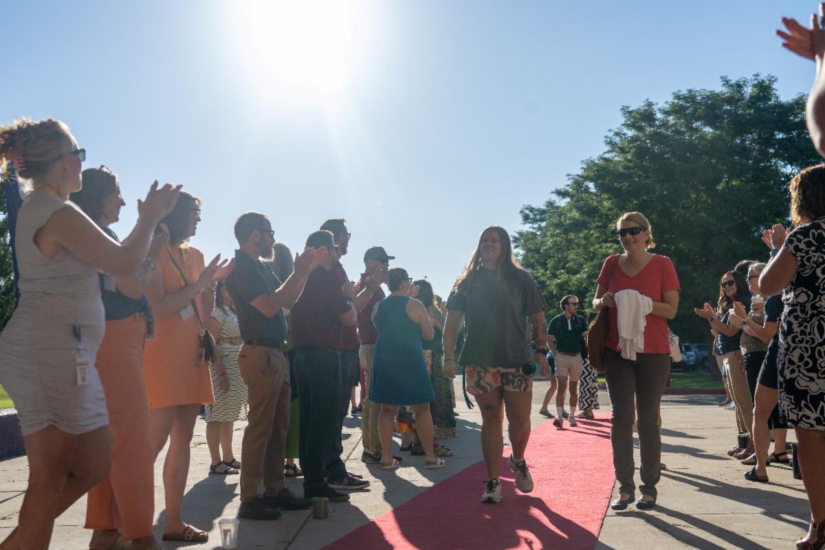 Educators cheer for teachers walking on a red carpet into a middle school for back to school professional development. 