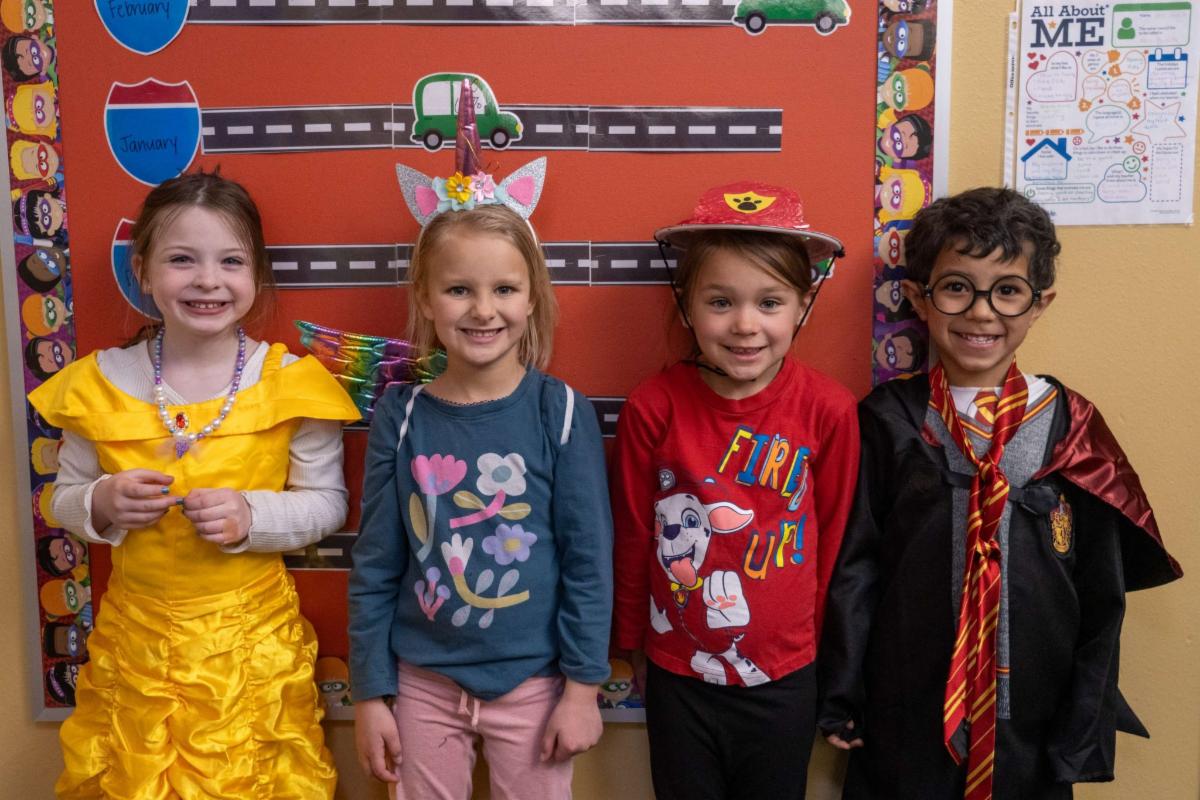 Four elementary school students stand in a row and smile at the camera. From left, they are dressed as Belle from Beauty and the Beast, a fairy unicorn, Marshal the fire pup from Paw Patrol, and Harry Potter.