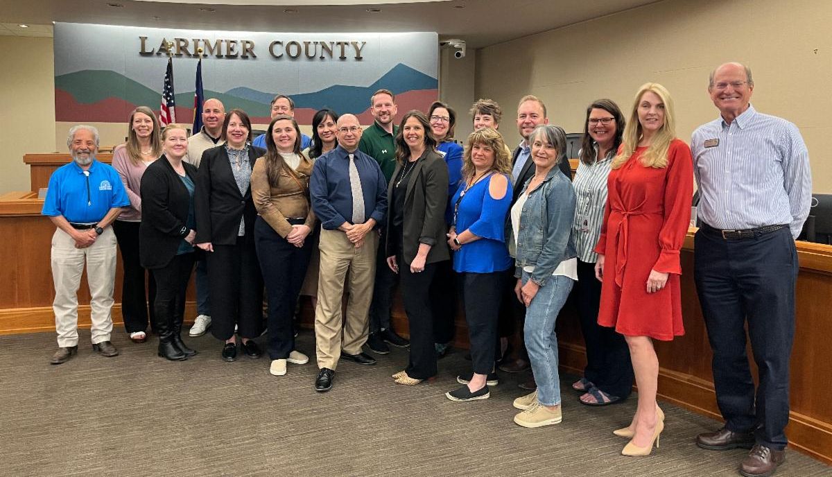  Diecinueve adultos posan para la cámara en la sala de reuniones de la junta de comisionados del condado.