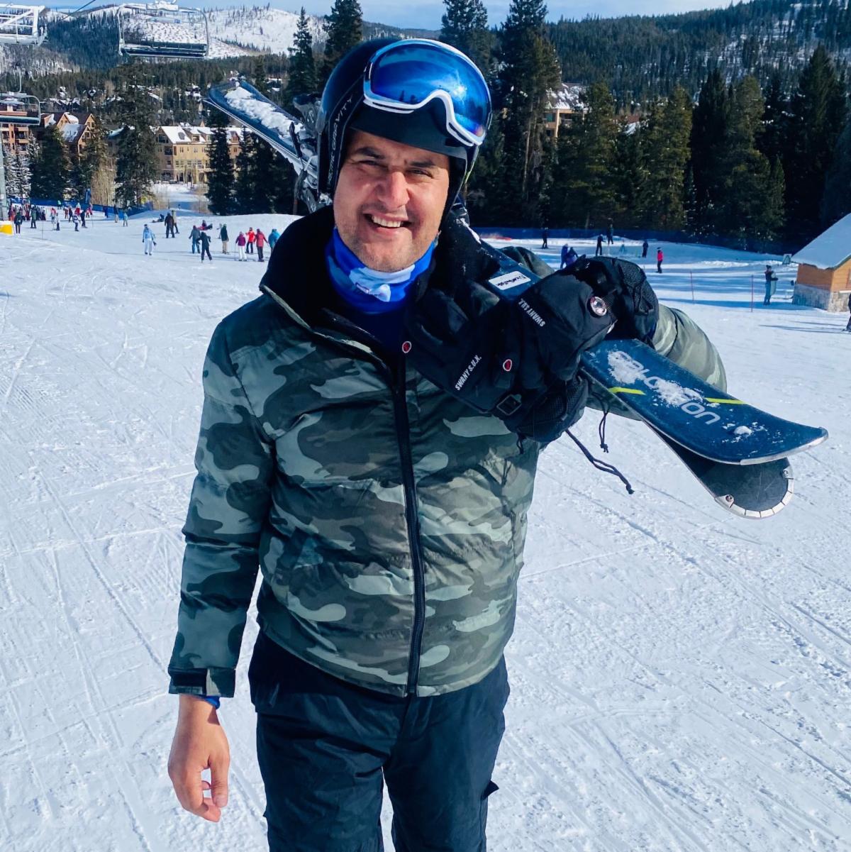 Najeeb Siddiqui outside on snow covered ski hill, carrying a set of skis