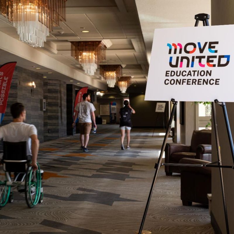 Conference attendees rolling and walking down the conference hallway sign in photo says Move United Education Conference