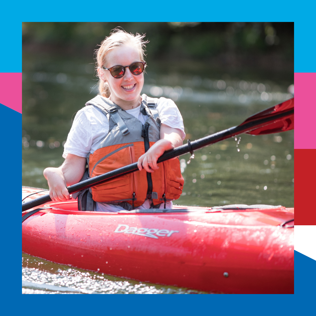 Adaptive kayaker smiling at camera while paddling downstream