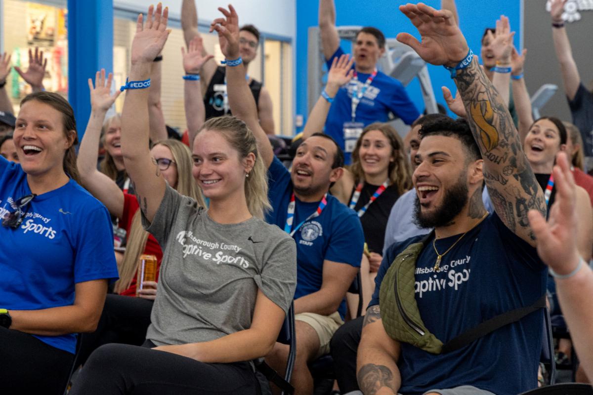 Several conference attendees seated in rows raising their hands with enthusiasm