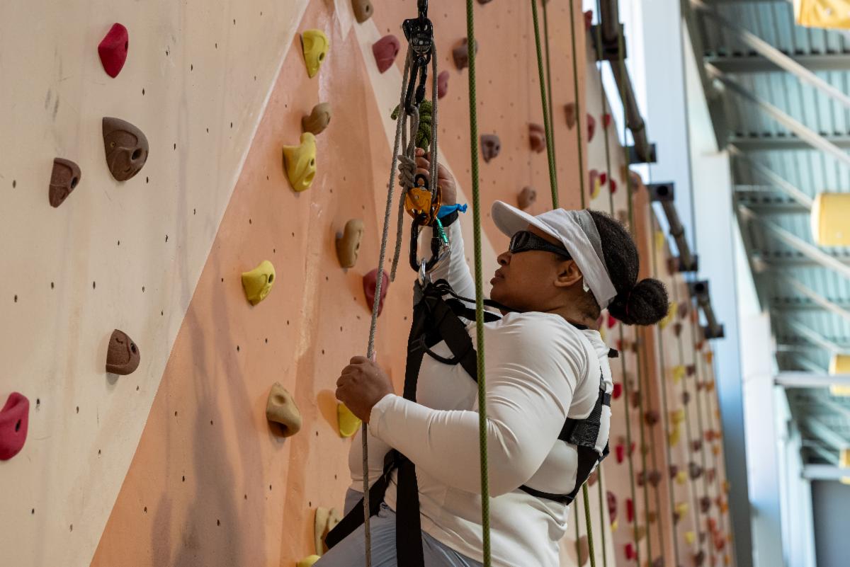 Visually impaired athlete in harness climbing up rock wall