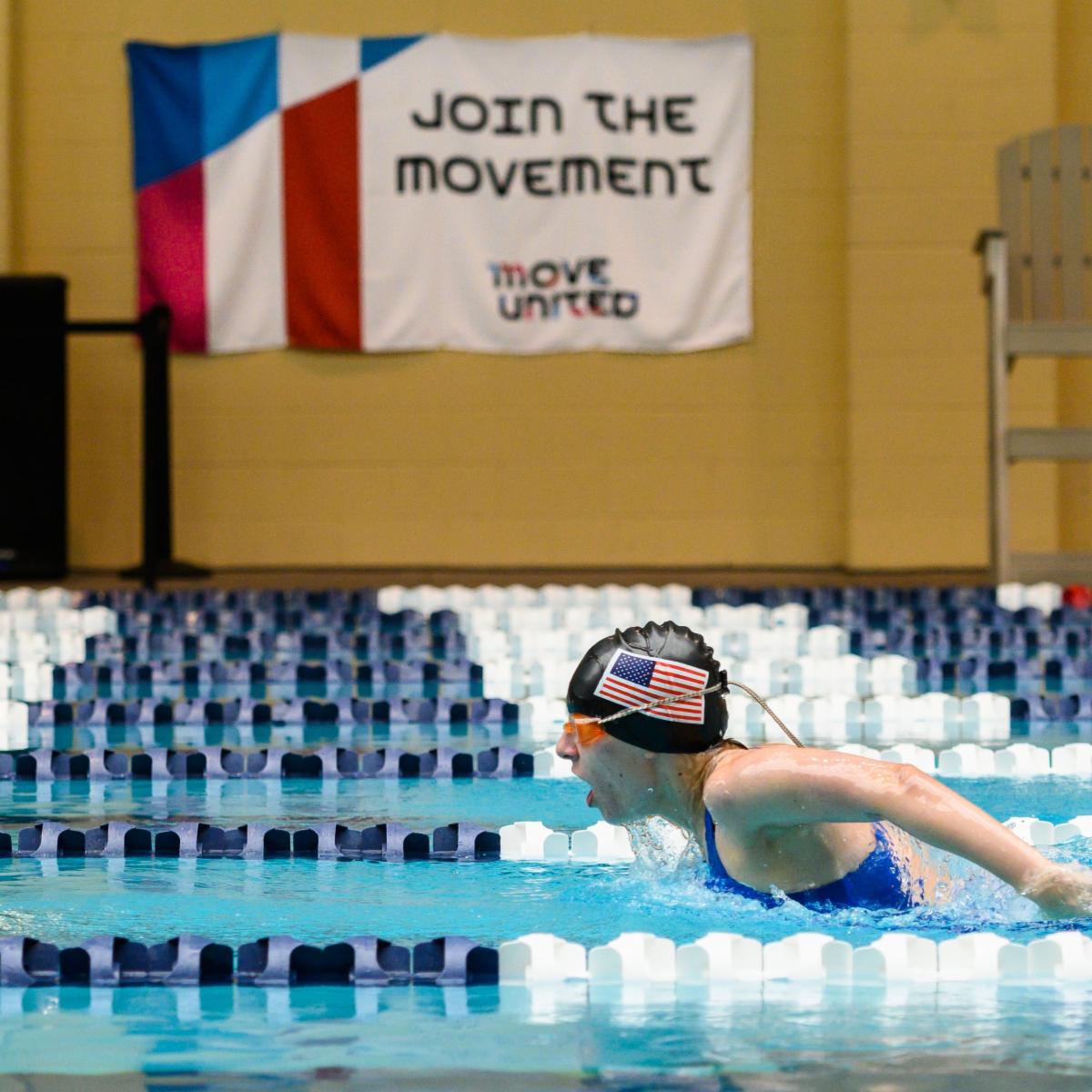 Swimmer in pool with "Join the Movement" on wall in the background