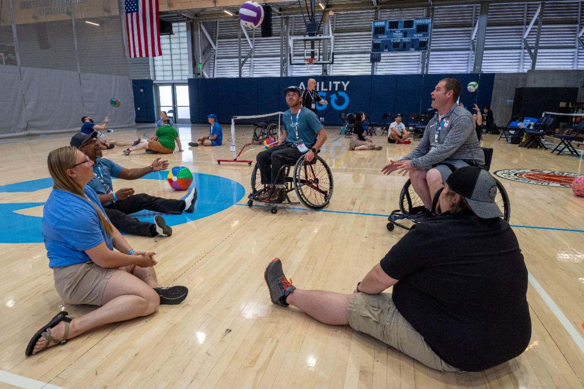 Several conference attendees either seated on gym floor or in chair passing volleyball to each other 