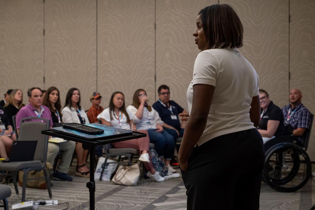 female presenter speaking at front of room to several conference attendees in her session