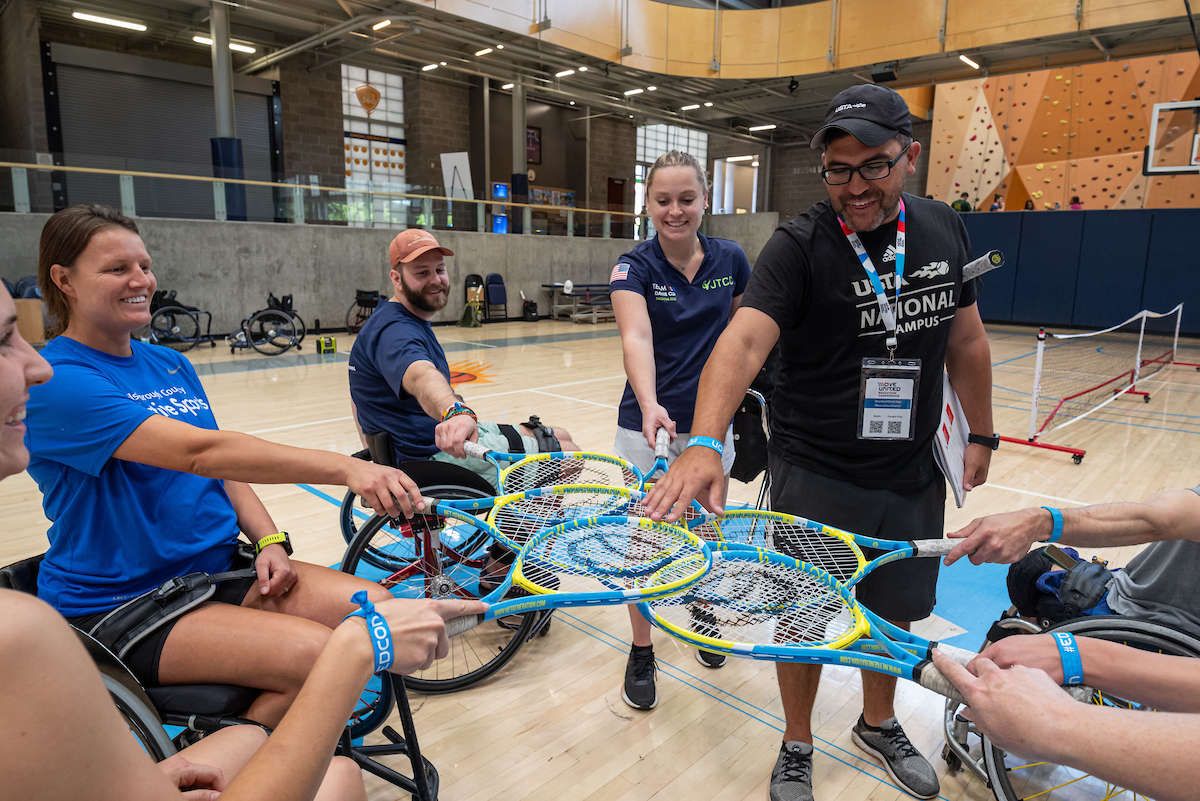 Session attendees on sport court holding rackets together in center of circle