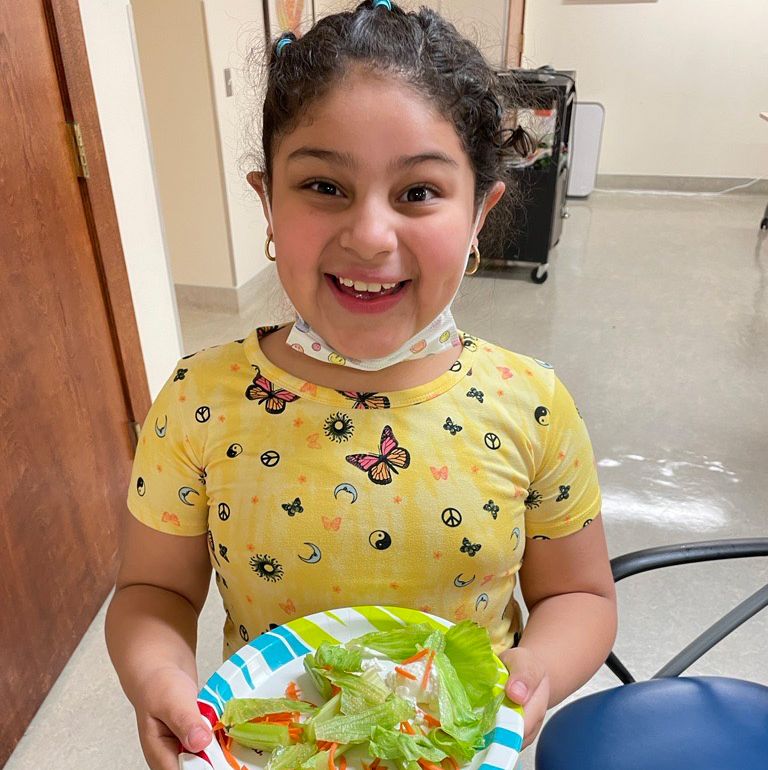 Girl with yellow shirt holds a plate with salad