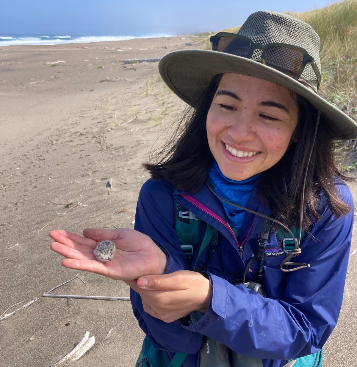 Aiko standing on a beach holding a small plover chick and smiling