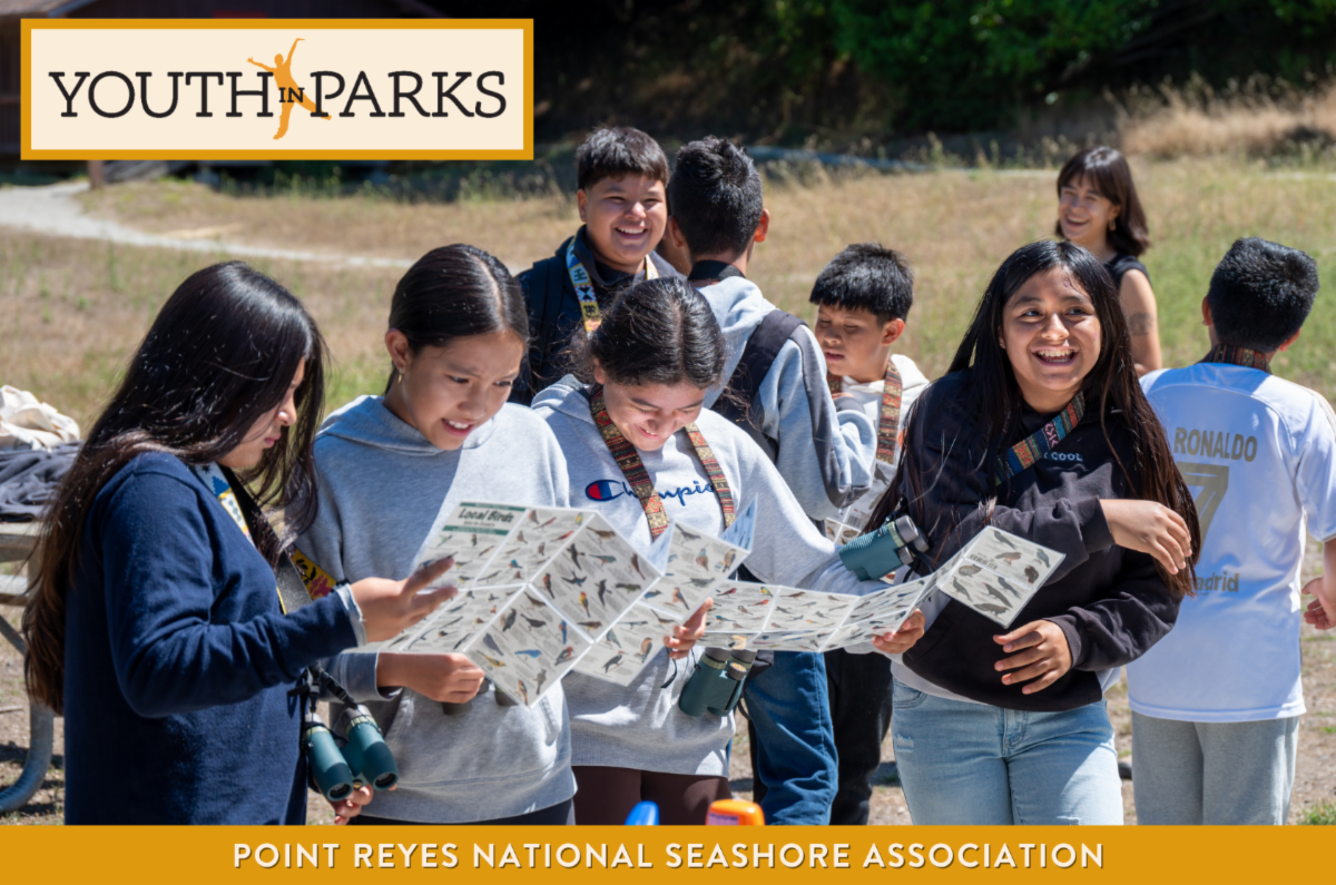 A group of youth outside looking at bird guides and laughing Text reads Youth in Parks and Point Reyes National Seashore Association