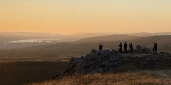 A group of people stand in the distance watching a golden sunset on the coast.