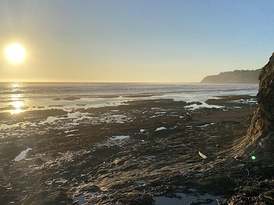 A landscape view of a sunset reflecting on tidepools and the vast ocean.