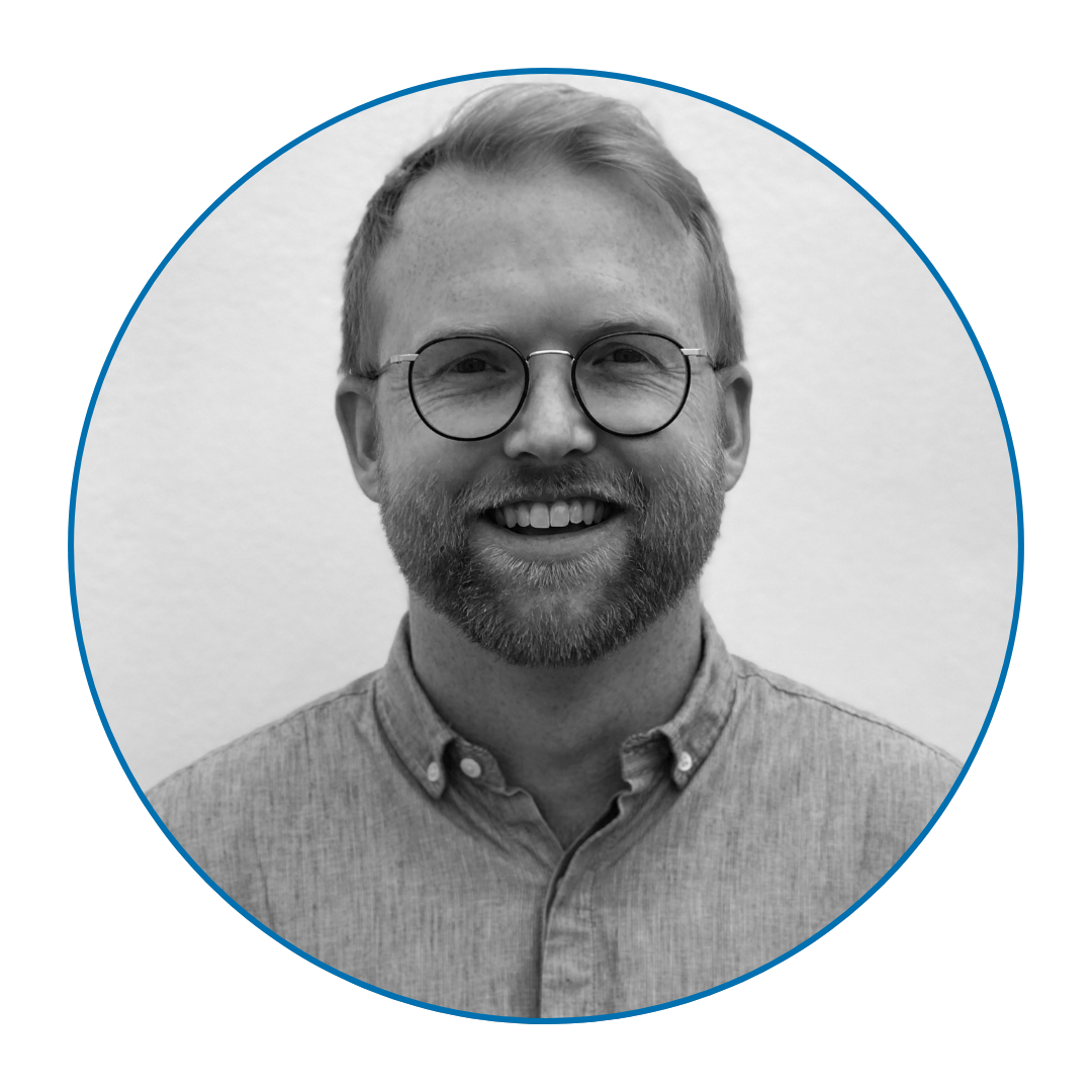 A black and white photo of a man smiling with short hair a beard and glasses