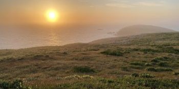 A hazy golden sunset over a rugged coast