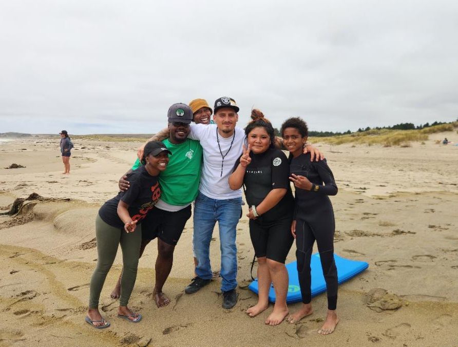 A group of young people smiling on a sandy beach with their arms around each other