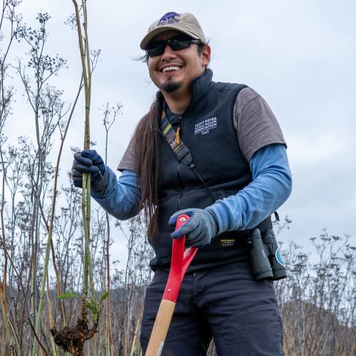 Cristobal smiling holding up fennel and a shovel.