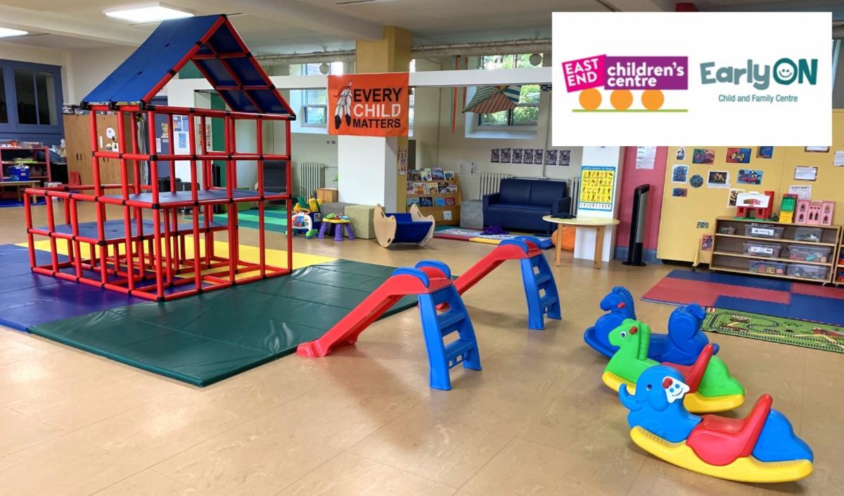 children's indoor play space with red climbing structure to the left and two toddler slides in the centre and three rocking horses to the right