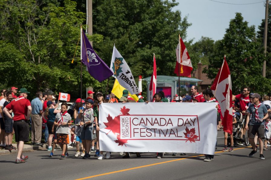 a crowd of people carrying the East York Canada Day banner in a parade environment