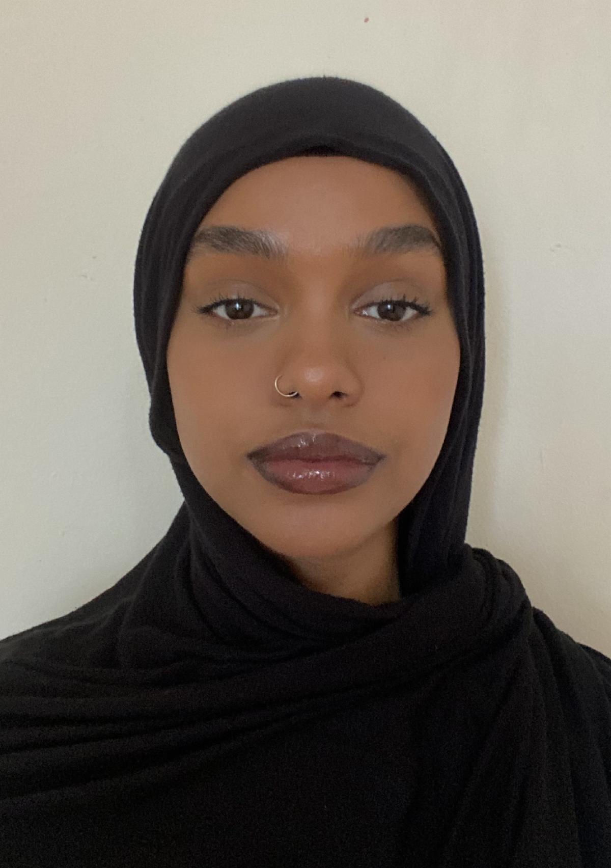 person dressed in black with a black head covering gazing calmly at the viewer