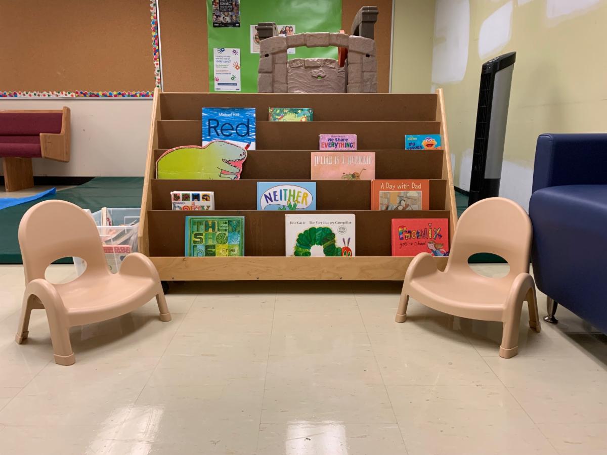 children's reading area with books arranged on a low shelf and two small beige toddle chairs on either side