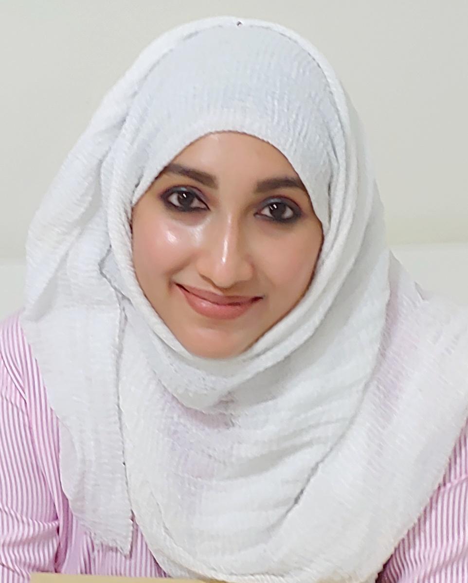 Female presenting person with light skin wearing a white head scarf smiles at the viewer