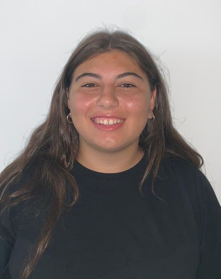 white person with long dark hair wearing a black t shirt gazes at the viewer with a friendly smile