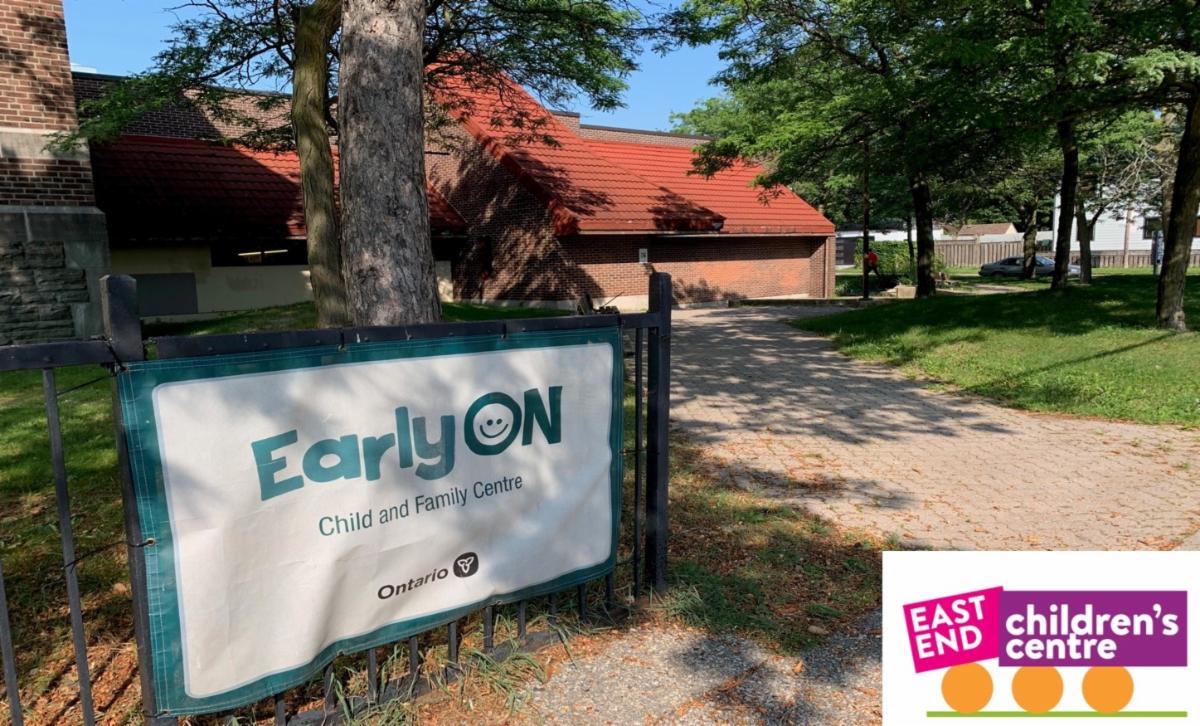 outdoor setting with pine trees around the entrance to a school and a sign reading EarlyON Child and Family Centre with an East End Children's Centre logo in the bottom right corner