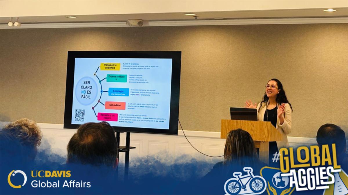 A speaker presents at a podium with a slide in Spanish displayed on a screen behind them and an audience seated in front. UC Davis Global Affairs and #GlobalAggies logos appears in the bottom corners.