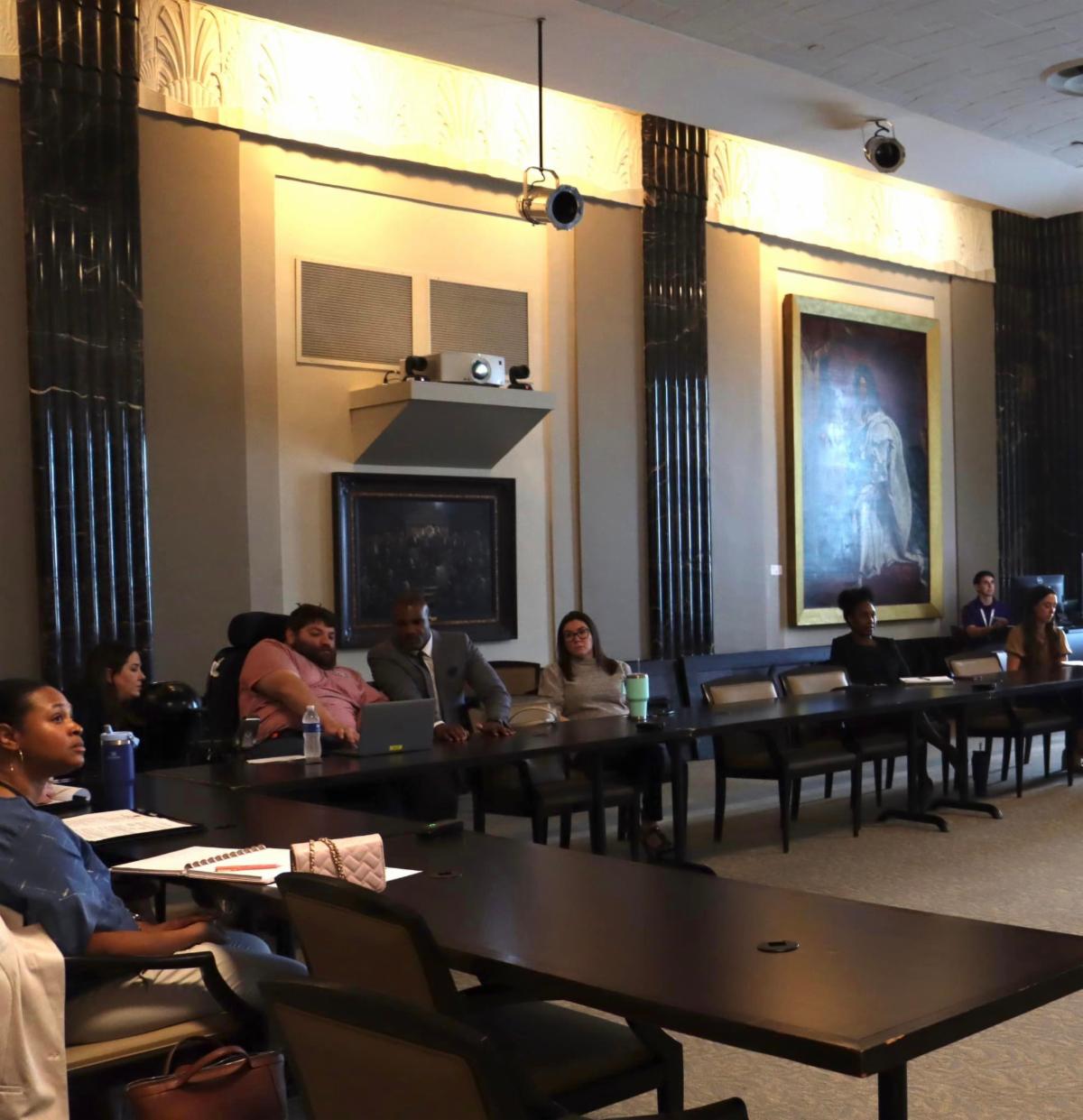 Picture is of a couple of people inside the press room at the state capitol who were present at the GACDA meeting sitting at tables listening to the presentation.