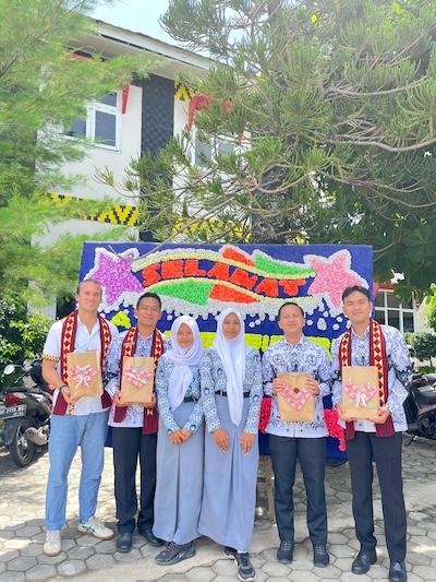 A group of people stand in an outdoor setting in front of a sign that says, Selamat