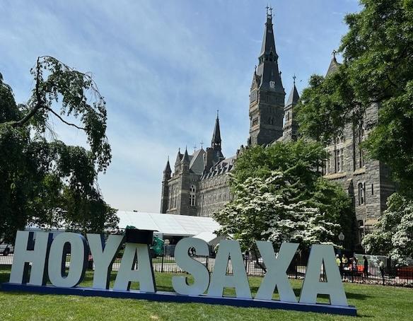 A large outdoor graduation sign that says Hoya Saxa in front of Healy Hall