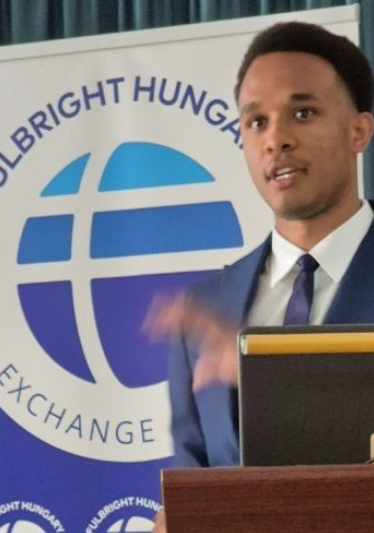 Noah Aire speaks at a podium with a Fulbright Hungary sign behind him