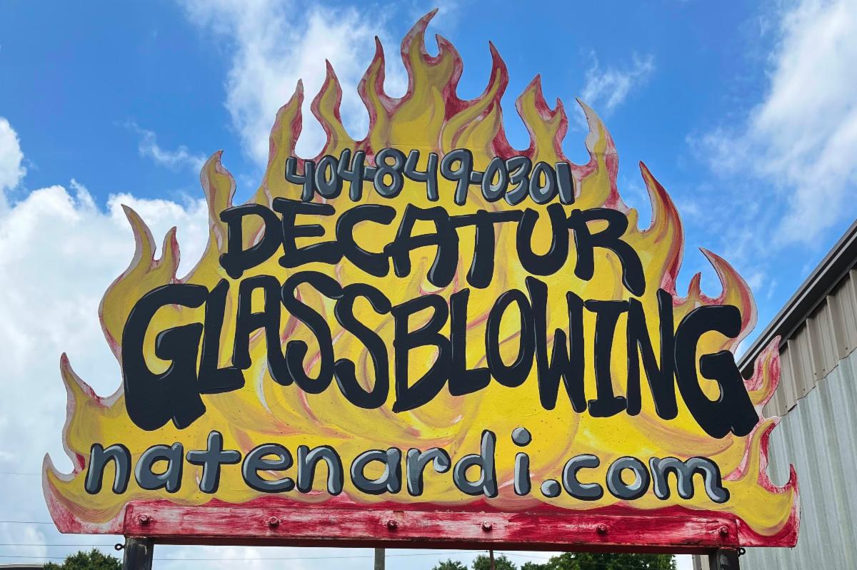 Decatur Glassblowing sign which is shaped like flames against a blue sky with clouds