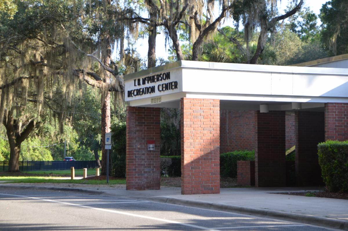 Exterior view of T.B. McPherson Recreation Center, a single-story brick building with a white canopy entrance, surrounded by greenery.