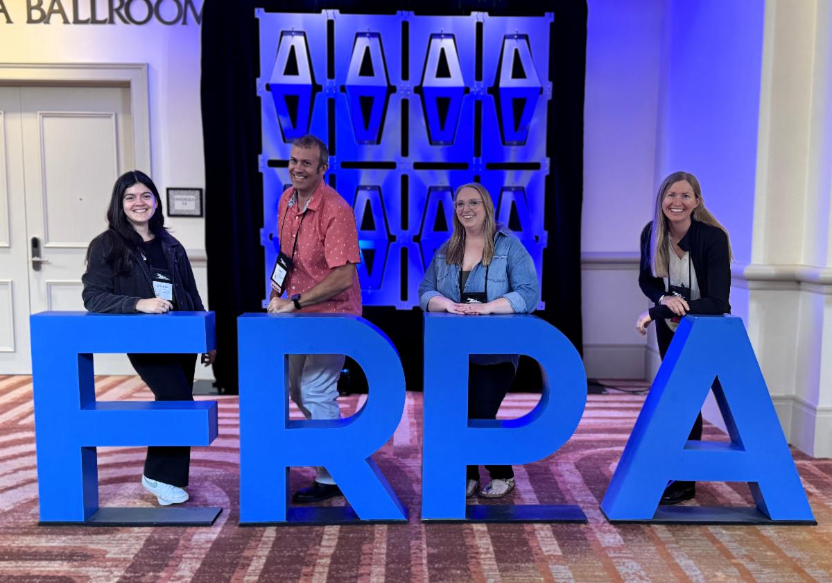 Four Wild Spaces and Public Places team members pose behind large blue “FRPA” letters at a conference.  Transcribed Text:  FRPA A BALLROOM MONICA 14