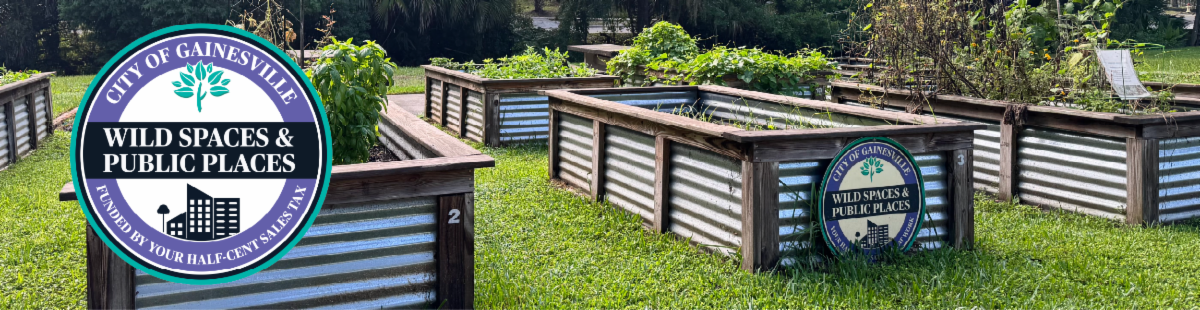 Raised garden beds with green plants and City of Gainesville “Wild Spaces & Public Places” signs.  Transcribed Text:  CITY OF GAINESVILLE WILD SPACES & PUBLIC PLACES FUNDED BY YOUR HALF-CENT SALESTAX YOUR TAXES AT WORK
