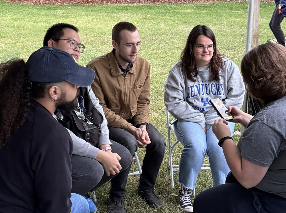 Graduate students hanging out underneath the tent at the tailgate.