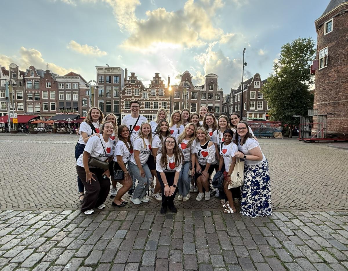 A pictures of Dr. Erin Richard with her summer study abroad students on cobblestone road with buildings in the background and the sun peeking through the buildings and clouds.