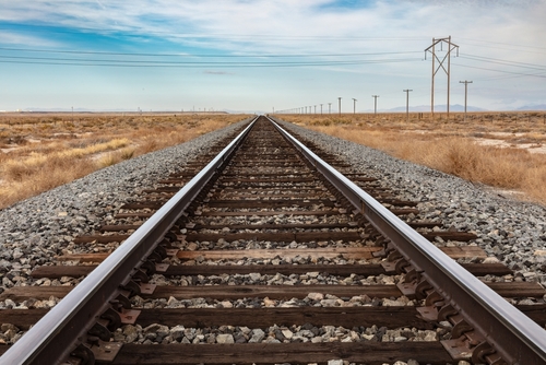Closeup of railroad tracksin central Utah. Stretching straight to the horizon. Telephone poles to the right. Blue cloudy sky beyond. 