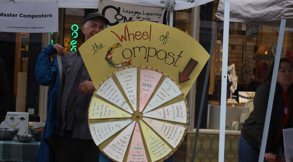 A person stands behind a spinning "Wheel of Compost," which is facts about the process not actual compost