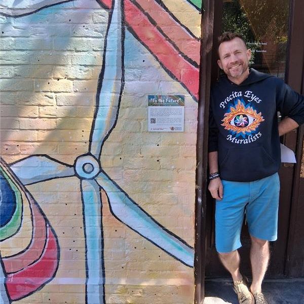A person stands in a doorway next to a mural wall including a wind turbine.
