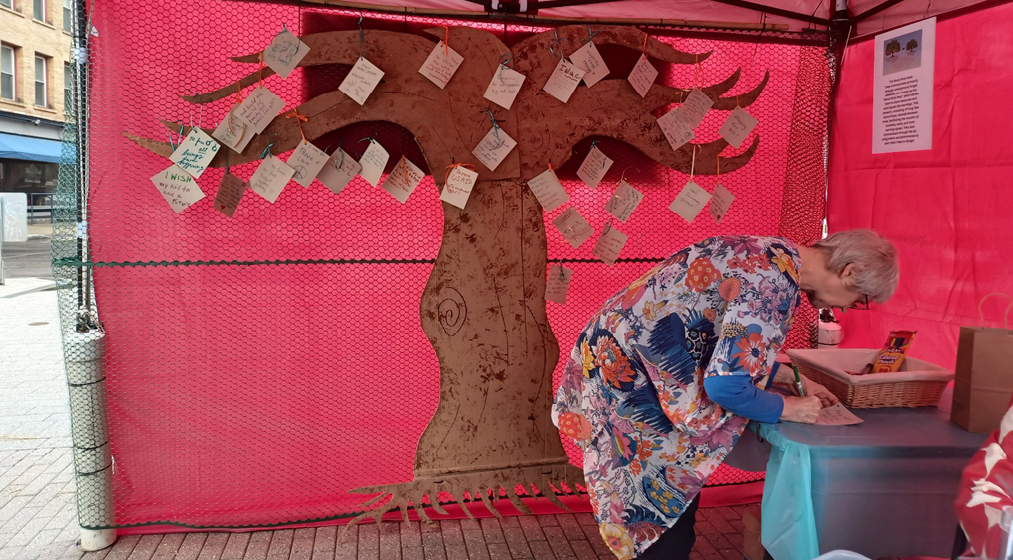 A person writing a note to add to a fabric tree hung with note cards.