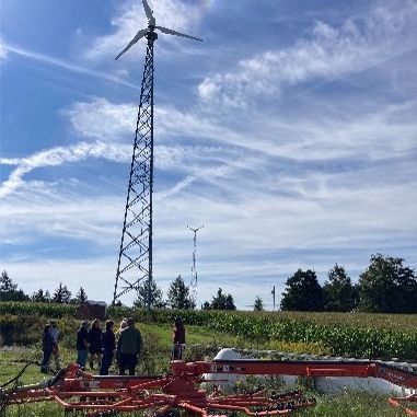 A group of people on a farm next to a tall windmill.