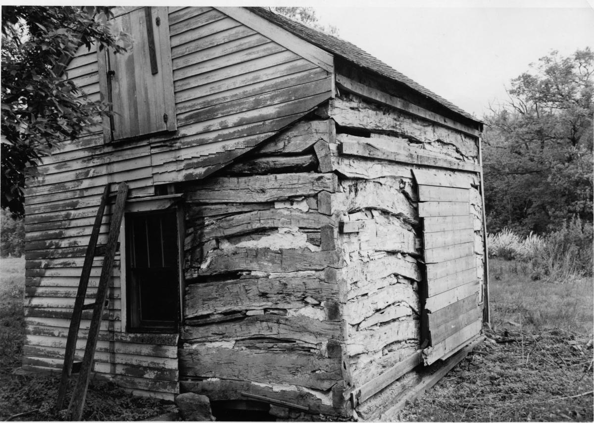 Black and white photo of the Palmer-Epard Cabin, a log cabin. Trees are visible in the background.